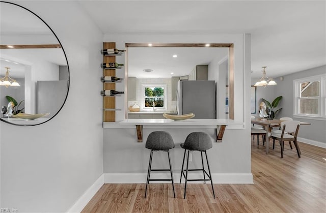 kitchen with a breakfast bar, light hardwood / wood-style floors, stainless steel refrigerator, and a notable chandelier