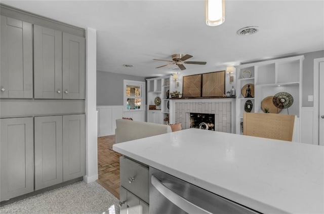 kitchen featuring gray cabinetry, ceiling fan, a brick fireplace, and light parquet flooring