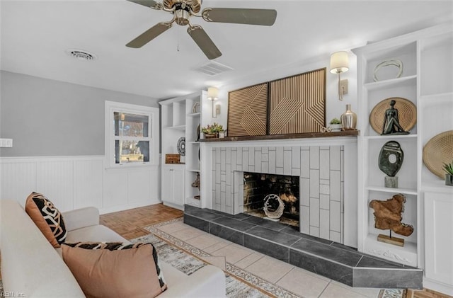 living room with built in shelves, ceiling fan, a tile fireplace, and light parquet floors