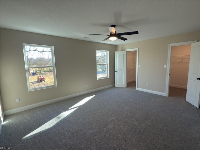 unfurnished bedroom featuring a walk in closet, a closet, dark carpet, and ceiling fan