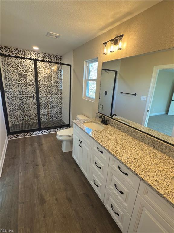 bathroom featuring a textured ceiling, vanity, a shower with door, hardwood / wood-style flooring, and toilet