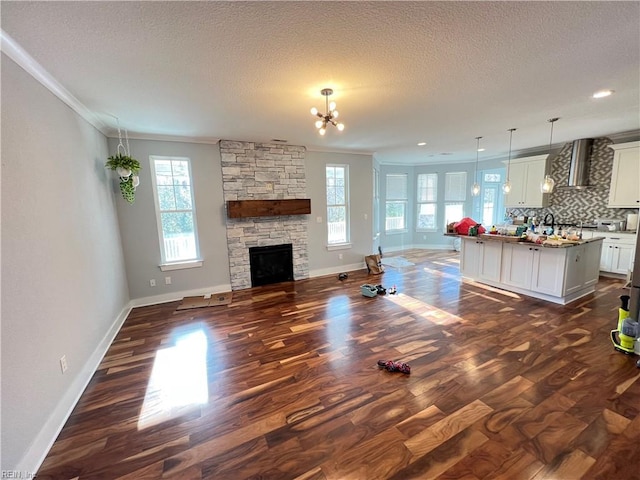 unfurnished living room with a stone fireplace, crown molding, dark hardwood / wood-style floors, and an inviting chandelier