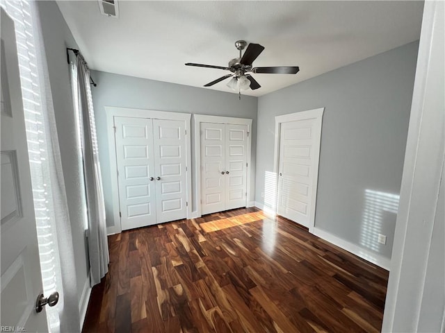 unfurnished bedroom with dark hardwood / wood-style flooring, ceiling fan, and multiple closets