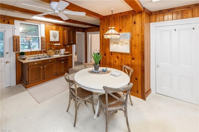 dining area with ceiling fan, wood walls, beam ceiling, and sink