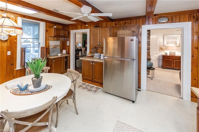 kitchen featuring ceiling fan, wooden walls, beam ceiling, decorative light fixtures, and stainless steel refrigerator