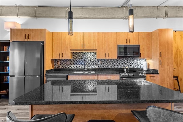 kitchen featuring dark stone countertops, sink, stainless steel appliances, and hanging light fixtures