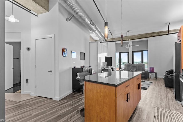 kitchen featuring wood-type flooring, decorative light fixtures, a kitchen island, and dark stone counters