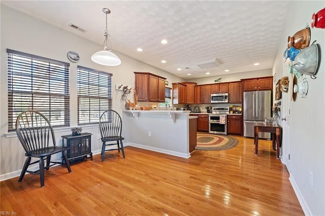 kitchen featuring pendant lighting, light wood-type flooring, appliances with stainless steel finishes, kitchen peninsula, and a breakfast bar area