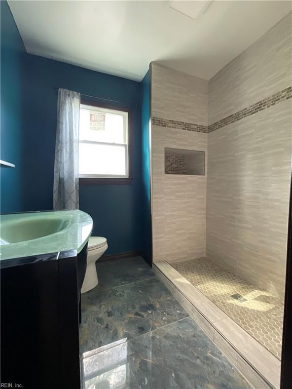 bathroom featuring a tile shower, vanity, and toilet