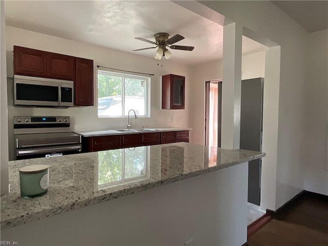 kitchen with light stone countertops, sink, ceiling fan, stainless steel appliances, and kitchen peninsula