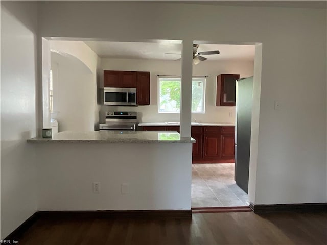 kitchen featuring kitchen peninsula, light stone countertops, stainless steel appliances, ceiling fan, and light hardwood / wood-style flooring