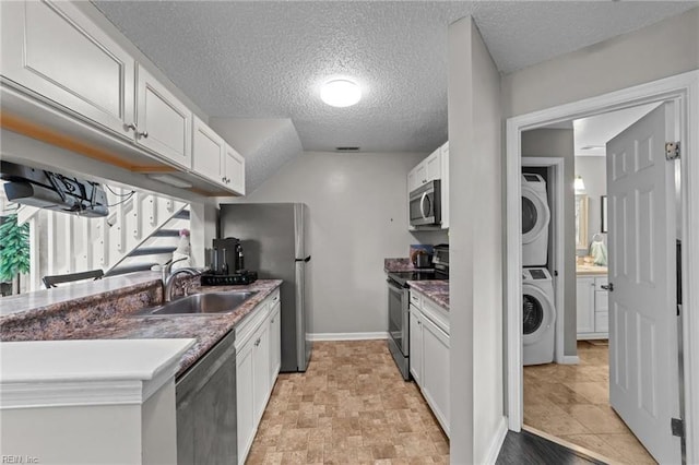 kitchen with white cabinets, sink, stacked washing maching and dryer, a textured ceiling, and stainless steel appliances