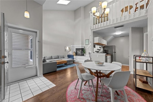 dining space featuring hardwood / wood-style floors, a notable chandelier, a towering ceiling, and a fireplace