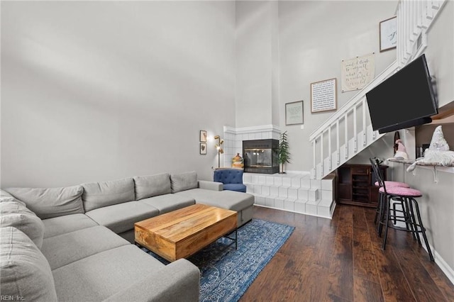 living room with dark hardwood / wood-style floors, a towering ceiling, and a tiled fireplace