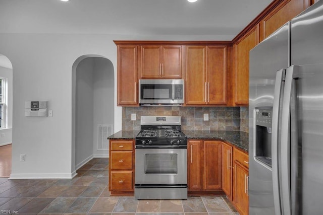 kitchen featuring stainless steel appliances, tasteful backsplash, and dark stone counters