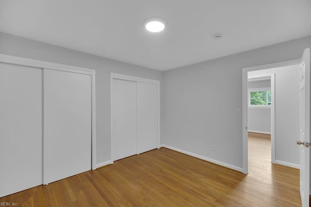 unfurnished bedroom featuring light wood-type flooring and multiple closets