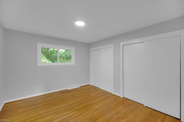 unfurnished bedroom featuring wood-type flooring and two closets