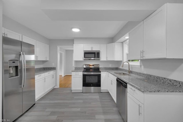 kitchen featuring white cabinets, sink, light stone countertops, appliances with stainless steel finishes, and light hardwood / wood-style floors