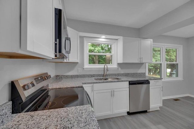 kitchen with appliances with stainless steel finishes, light stone counters, sink, light hardwood / wood-style flooring, and white cabinetry