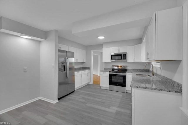 kitchen with appliances with stainless steel finishes, light hardwood / wood-style flooring, white cabinetry, and sink