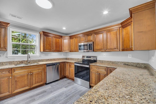 kitchen featuring light stone countertops, sink, crown molding, light hardwood / wood-style floors, and appliances with stainless steel finishes