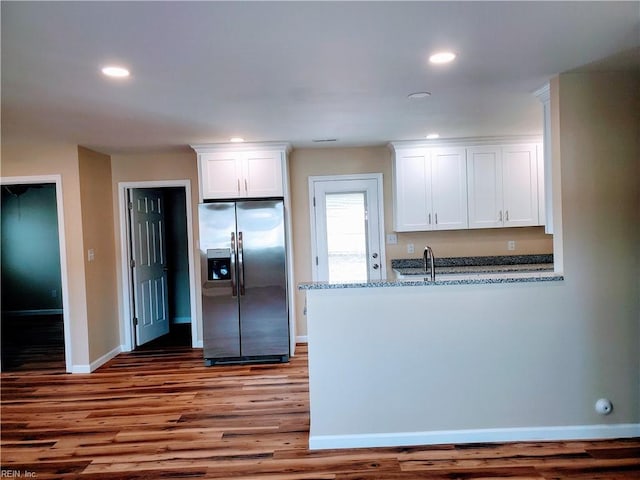 kitchen with light stone countertops, white cabinetry, sink, stainless steel refrigerator with ice dispenser, and wood-type flooring