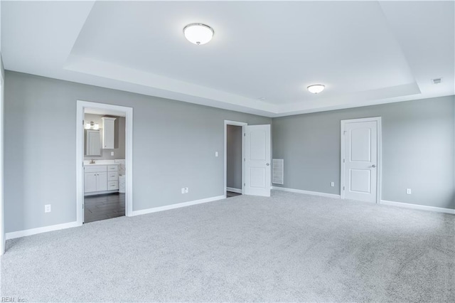 unfurnished bedroom with carpet flooring, connected bathroom, and a tray ceiling