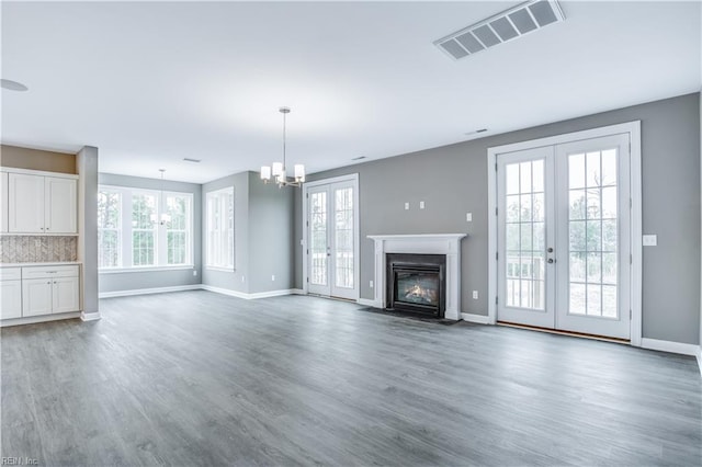 unfurnished living room featuring a chandelier, a healthy amount of sunlight, dark hardwood / wood-style flooring, and french doors