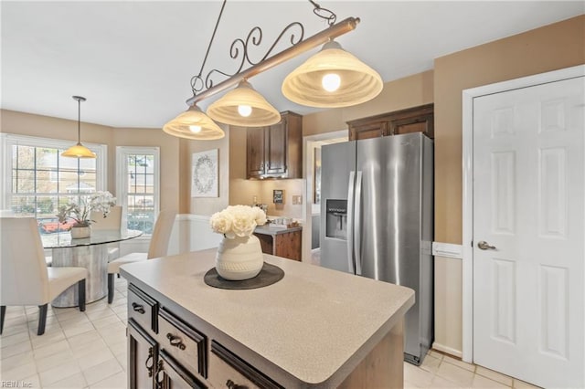 kitchen with hanging light fixtures, light tile patterned flooring, stainless steel refrigerator with ice dispenser, dark brown cabinets, and a kitchen island