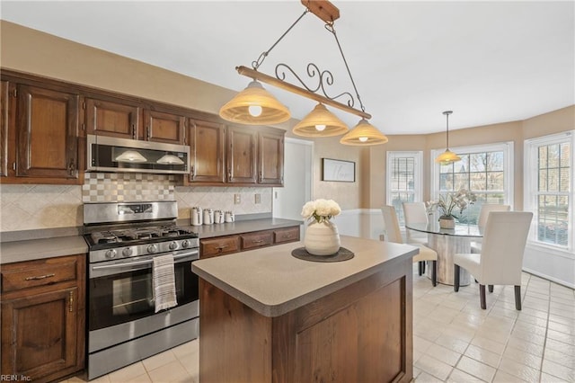 kitchen with a center island, hanging light fixtures, light tile patterned floors, tasteful backsplash, and stainless steel appliances