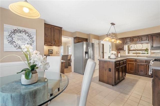 kitchen with backsplash, sink, stainless steel fridge with ice dispenser, a kitchen island, and hanging light fixtures