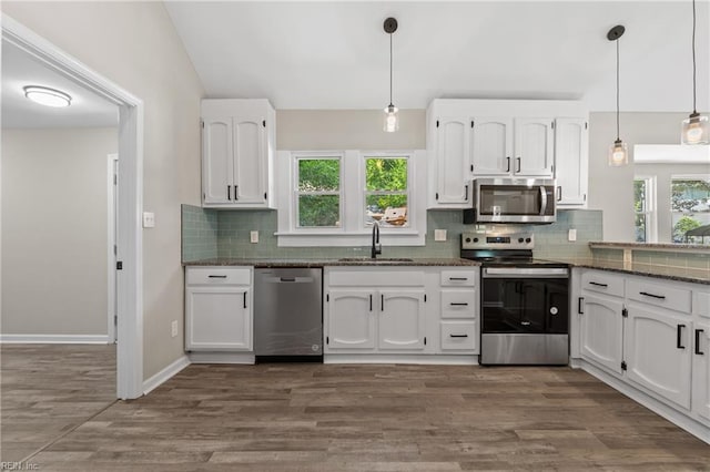 kitchen featuring stainless steel appliances, sink, pendant lighting, dark stone countertops, and white cabinets