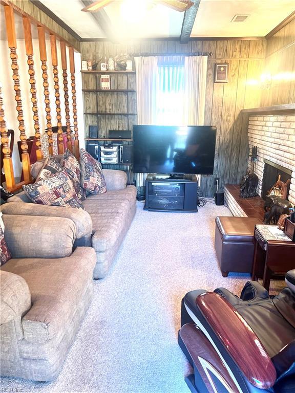 carpeted living room with beam ceiling, a brick fireplace, and wooden walls