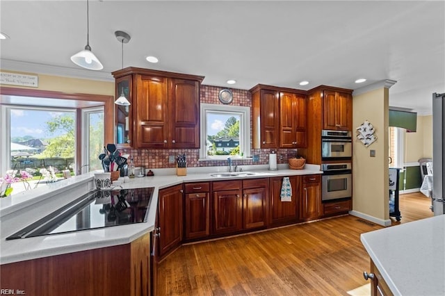 kitchen with light wood-type flooring, black electric cooktop, double oven, sink, and pendant lighting