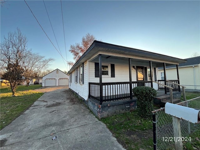 bungalow-style house featuring a porch, a garage, an outbuilding, and a front lawn