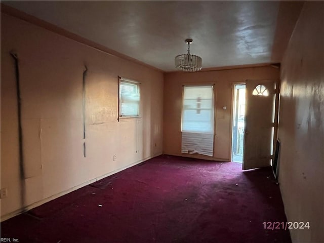 unfurnished room featuring an inviting chandelier, a healthy amount of sunlight, and dark colored carpet