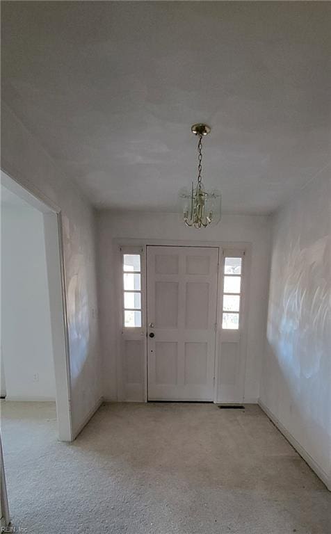 carpeted foyer entrance featuring a notable chandelier and a healthy amount of sunlight