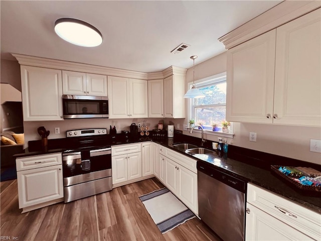 kitchen featuring appliances with stainless steel finishes, dark hardwood / wood-style flooring, sink, white cabinets, and hanging light fixtures