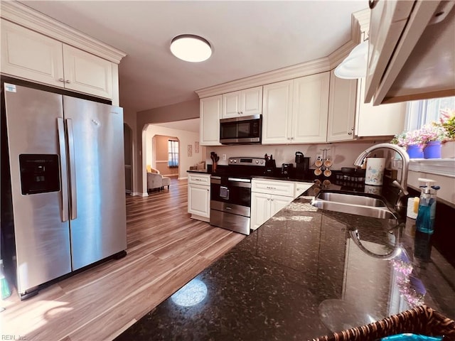 kitchen featuring dark stone counters, white cabinets, sink, light hardwood / wood-style flooring, and stainless steel appliances