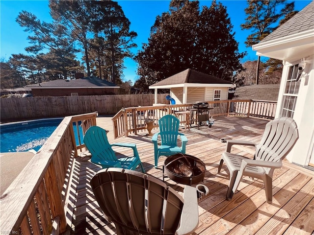 deck featuring a fire pit, a grill, a fenced in pool, and an outbuilding