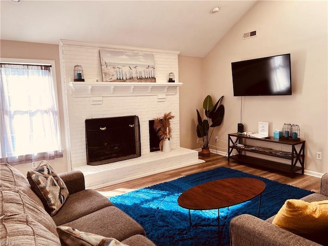 living room with hardwood / wood-style floors, vaulted ceiling, a brick fireplace, and a wealth of natural light