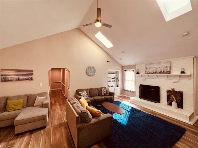 living room featuring high vaulted ceiling, a skylight, ceiling fan, a fireplace, and wood-type flooring