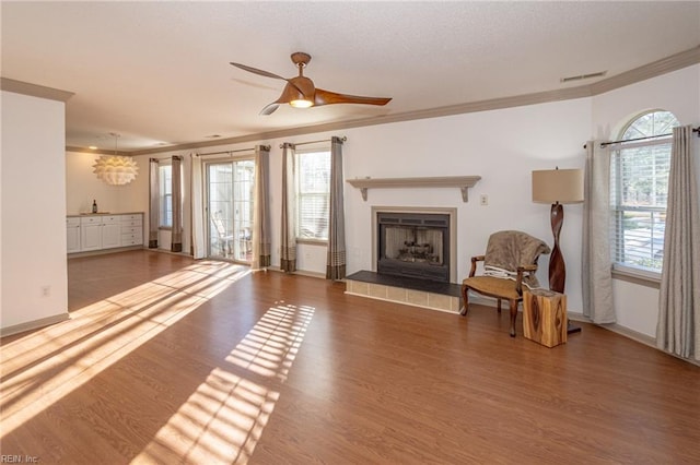 living room featuring crown molding, a fireplace, wood-type flooring, and ceiling fan with notable chandelier