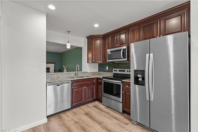 kitchen with pendant lighting, sink, decorative backsplash, light stone countertops, and appliances with stainless steel finishes