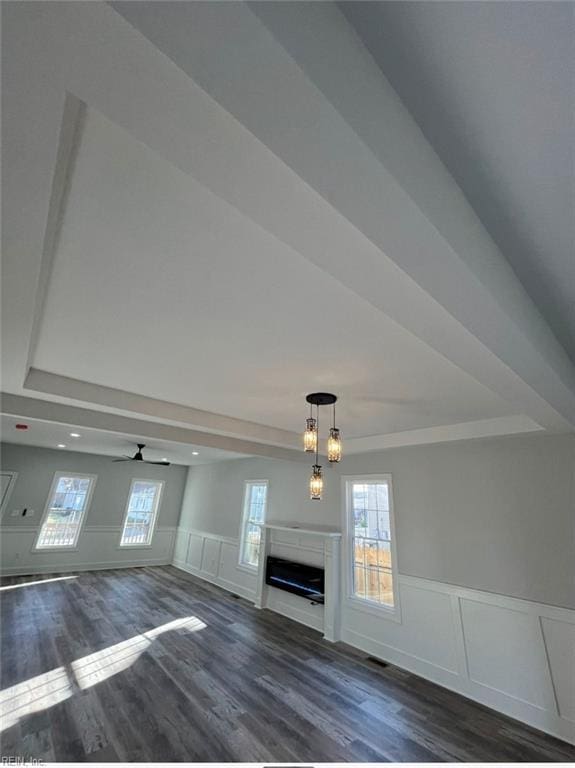 unfurnished living room with dark hardwood / wood-style flooring, ceiling fan with notable chandelier, and a tray ceiling