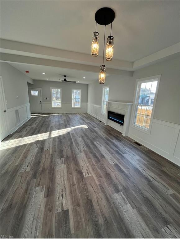 unfurnished living room featuring ceiling fan with notable chandelier, dark hardwood / wood-style floors, and a wealth of natural light