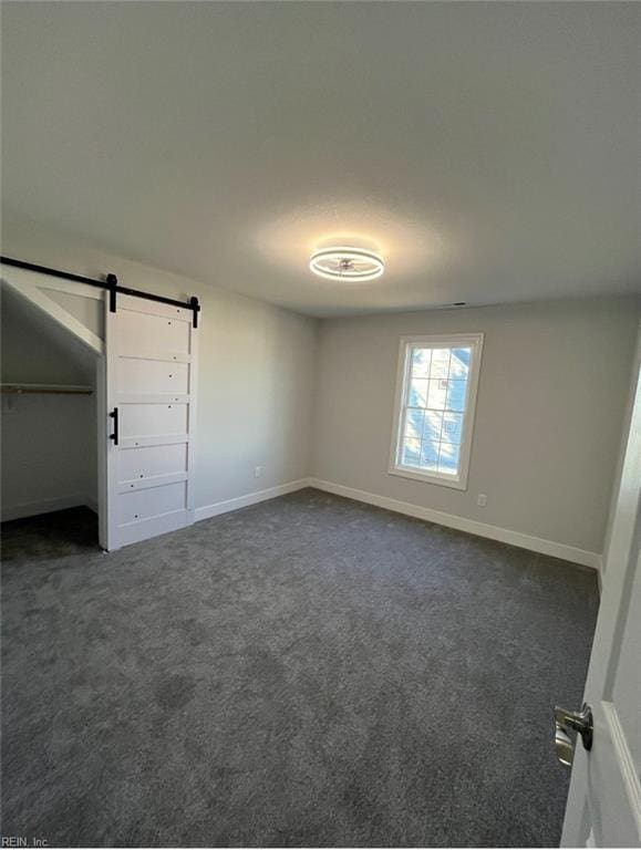 unfurnished bedroom featuring dark colored carpet and a barn door