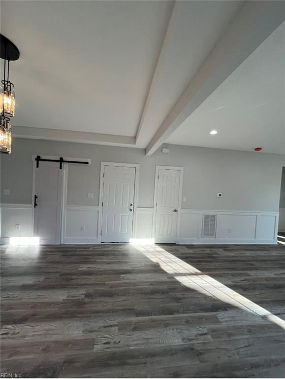 interior space with dark hardwood / wood-style flooring, a barn door, and beam ceiling