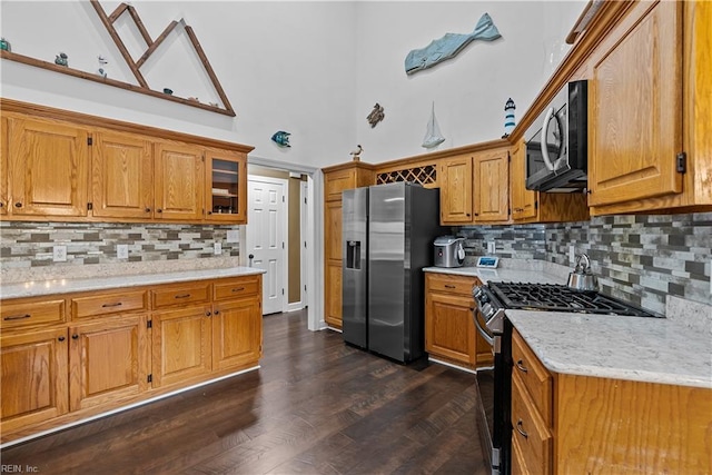 kitchen with light stone countertops, high vaulted ceiling, dark hardwood / wood-style floors, backsplash, and appliances with stainless steel finishes