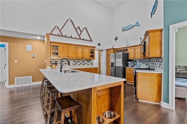 kitchen with a kitchen bar, a high ceiling, sink, appliances with stainless steel finishes, and dark hardwood / wood-style flooring